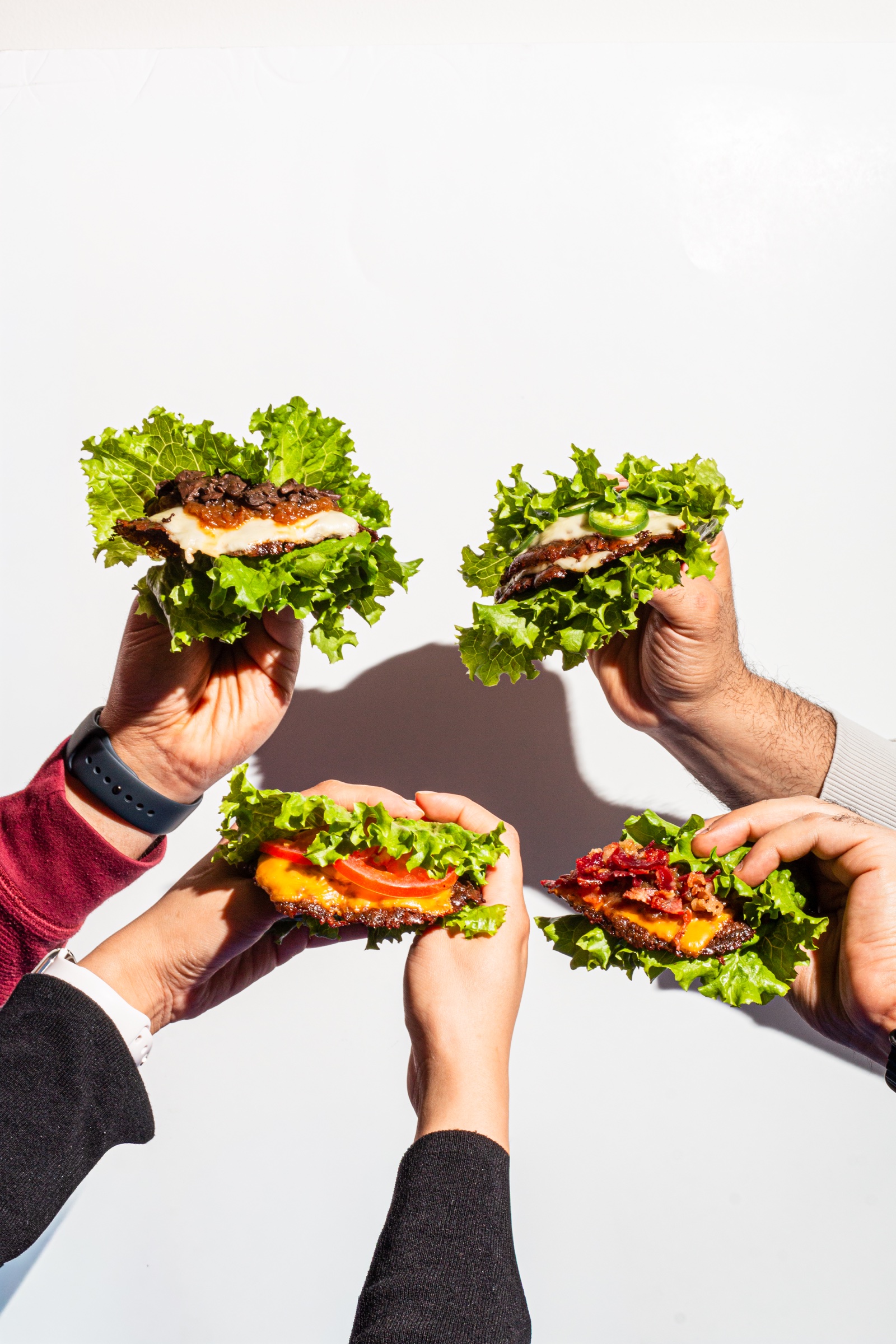 Friends raising colorful lettuce-wrapped burgers for Halal Smash BRGR