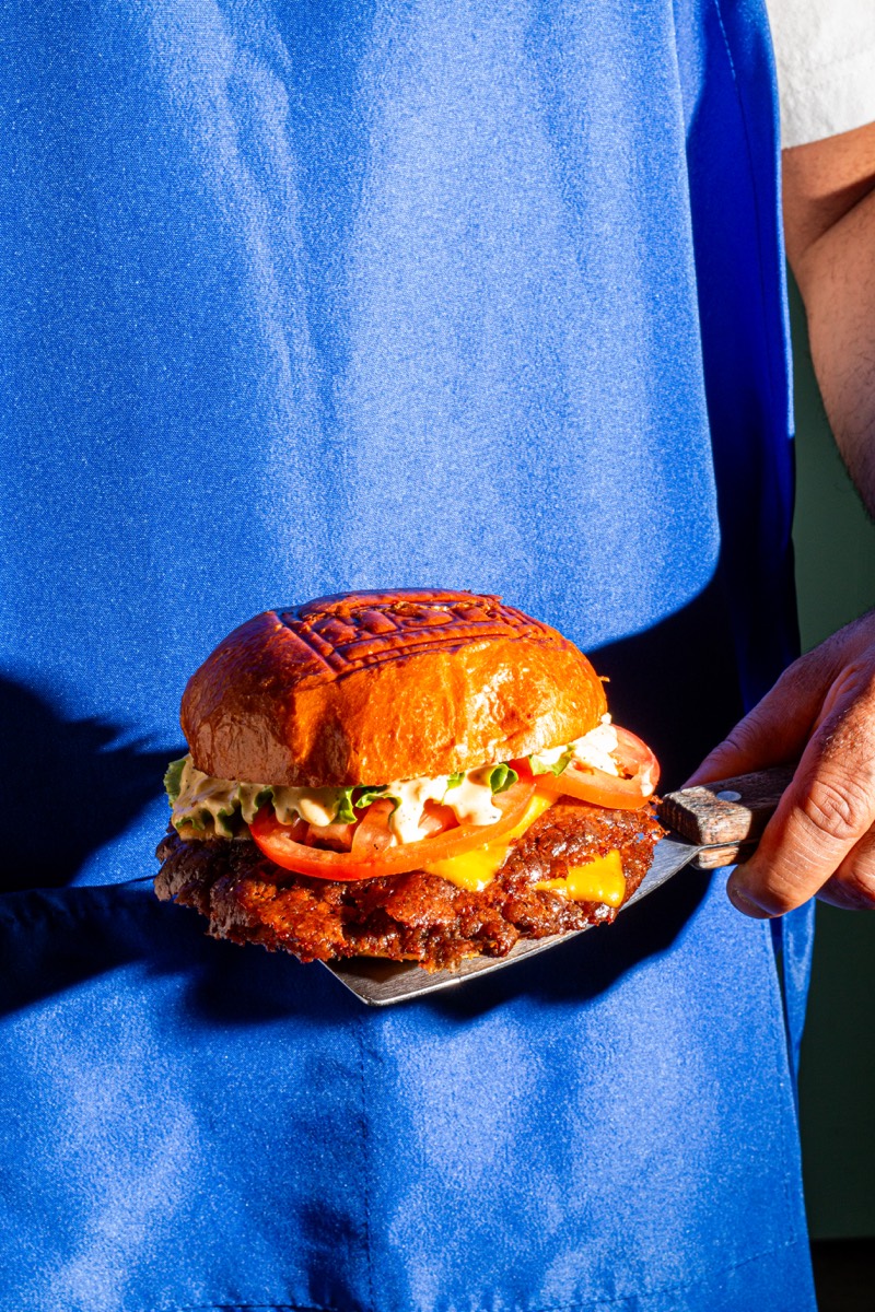 Smash burger presented on a spatula against a blue apron