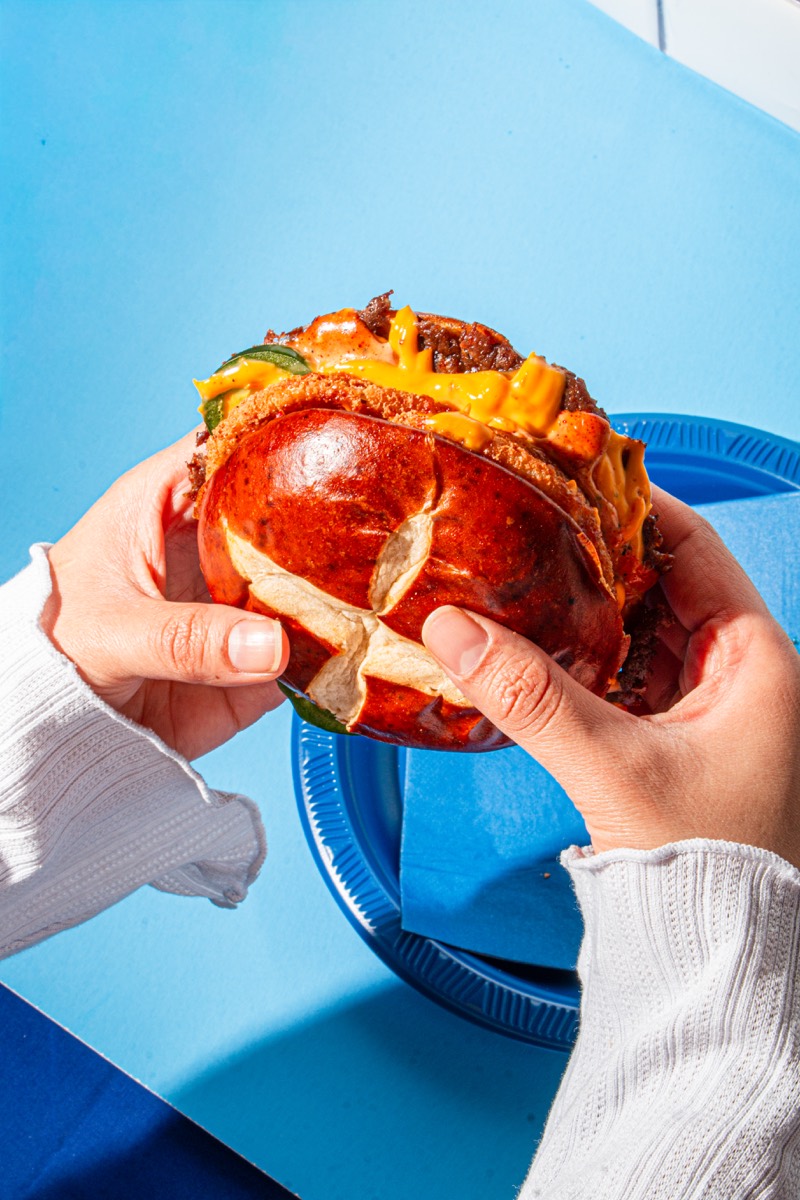 Hands holding a smash burger over a bright blue table
