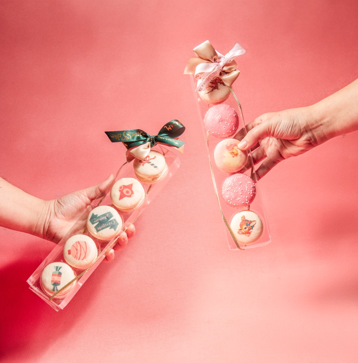 Hands holding holiday macaron gift boxes on pink