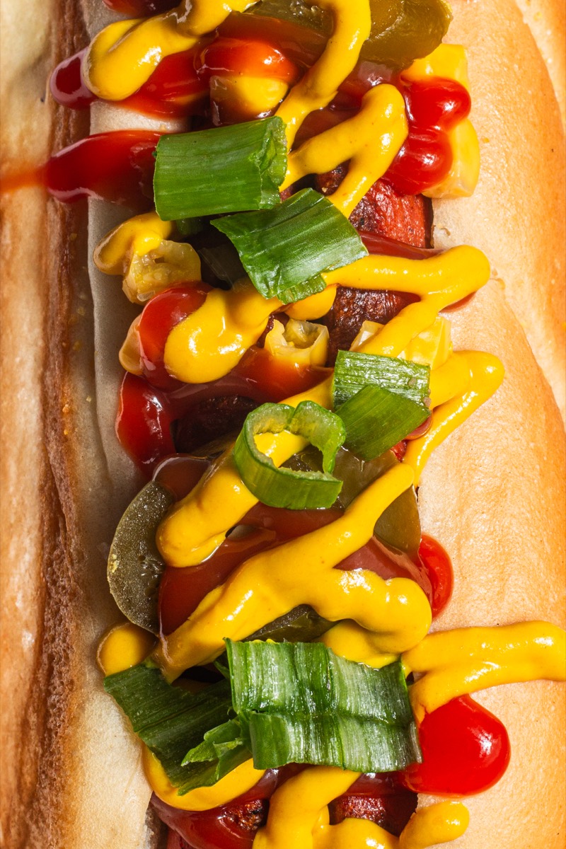 Close-up hot dog with mustard, ketchup, jalapeños and scallions