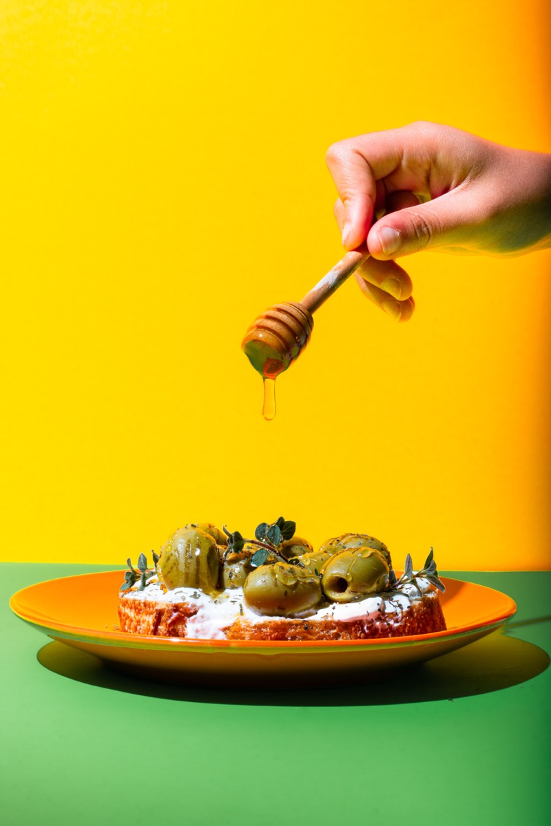 Olive toast with a honey drizzle on a vivid yellow and green set