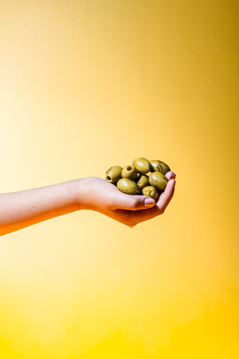 Handful of green olives against a yellow background