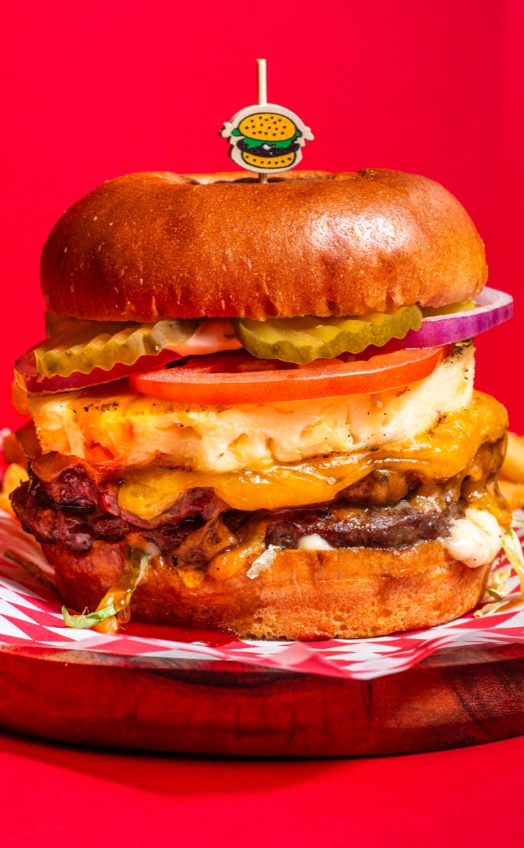 A towering stack of four glossy smash burgers against vivid blue