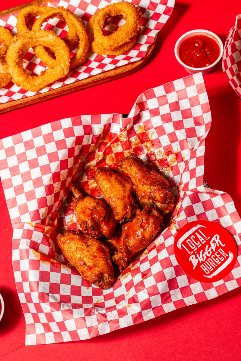 Saucy wings with onion rings on a bold red tabletop