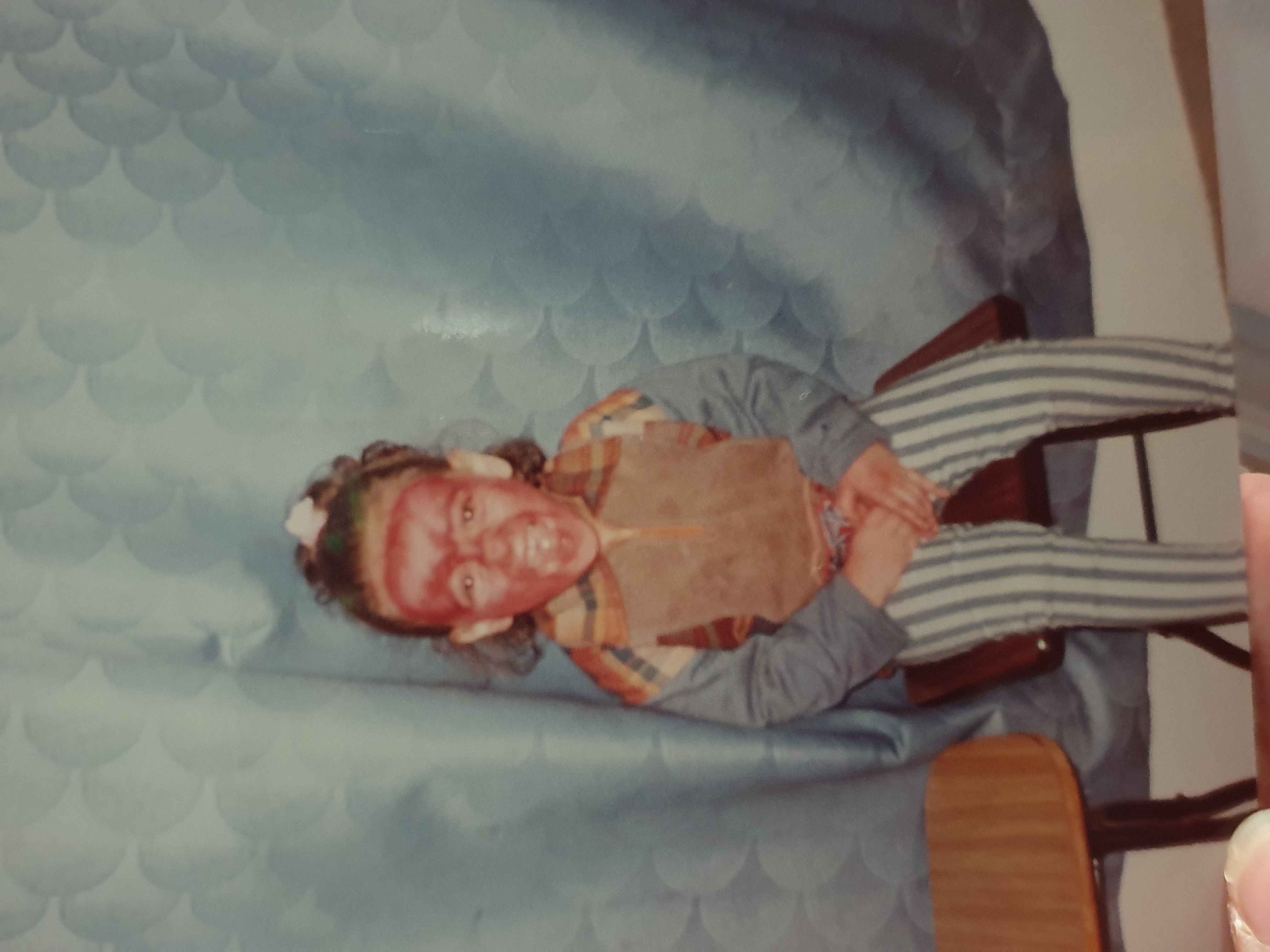 Yasmin as a child, smiling with red face paint while seated in front of a blue curtain